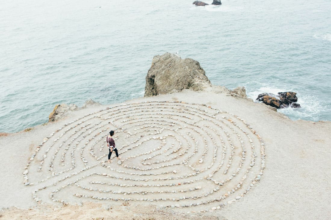 Person geht durch ein Steinlabyrinth an der Küste, ein Sinnbild für den Weg im Coaching